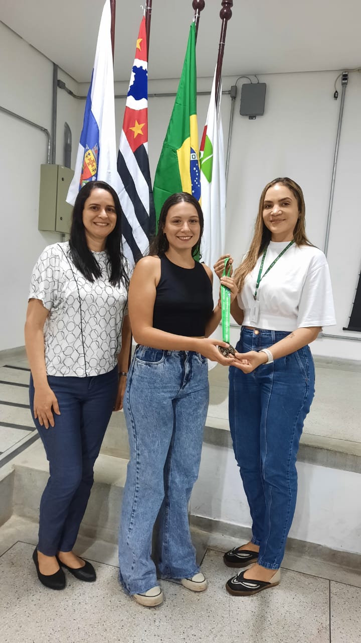 Diretora Juliana (à direita) entregando a medalha para a aluna Sophia (ao centro), com a prof. Samara (à esquerda).