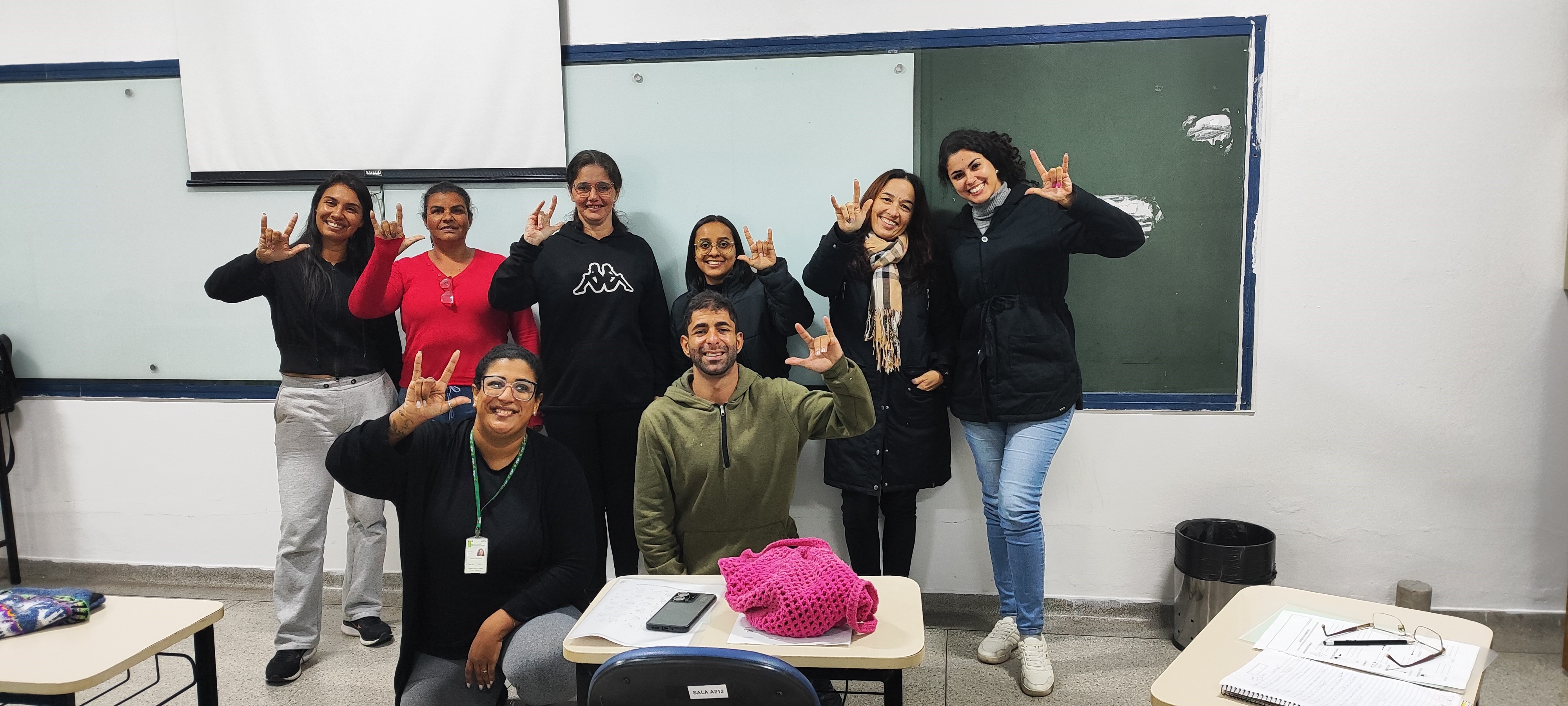 Imagem 15: Foto final com as alunas, a professora Izabela e Lucas fazendo o sinal “ILY” (“I love you” em ASL), gesto afetivo amplamente usado na cultura surda, embora não pertença à Libras.