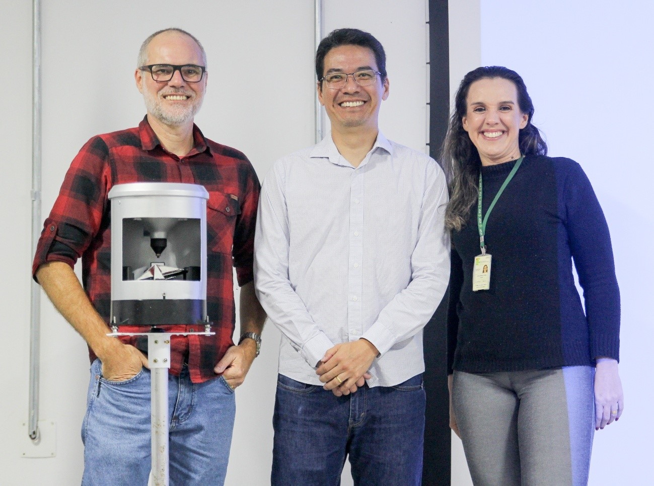 Imagem 3: Da esquerda para a direita: Prof. Dr. Ederson Rafael Wagner, Dr. Rogério Ishibashi e Profa. Ma. Juliana Matheus Grégio Pereira, coordenadora do curso de ADS do IFSP-CAR. À frente, o pluviômetro de báscula utilizado na demonstração durante a palestra do Cemaden na SNCT 2025.