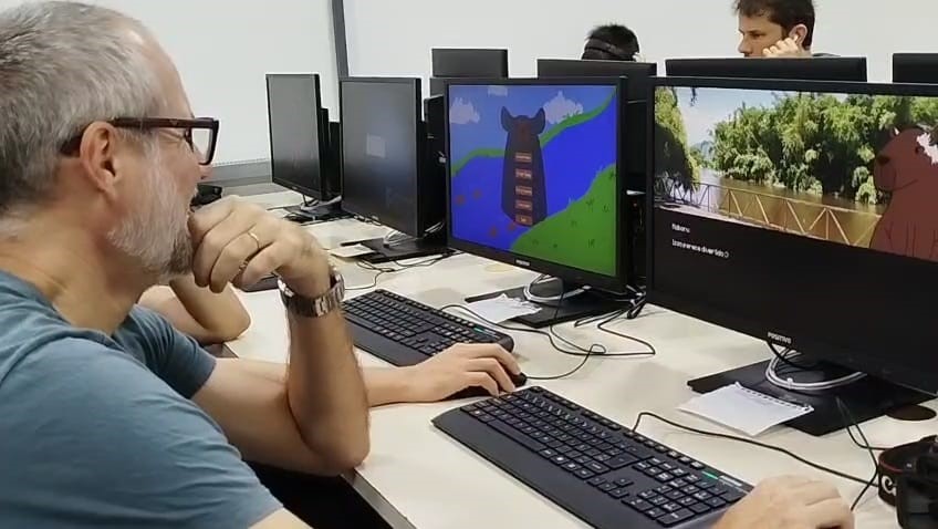 Imagem 3: Prof. Ederson, responsável pela cobertura fotográfica do evento, em primeiro plano e Prof. Renan ao fundo, membro da Comissão Organizadora do Game Jam 2025, durante Mostra Interativa.