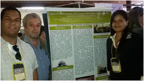 João, professor Ricardo e Ariane junto ao pôster sobre Kepler e a gravidade