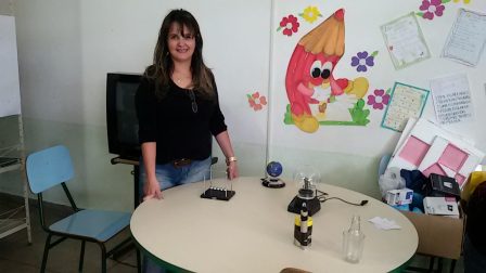 Adriana na mesa com experimentos de física para serem manipulados